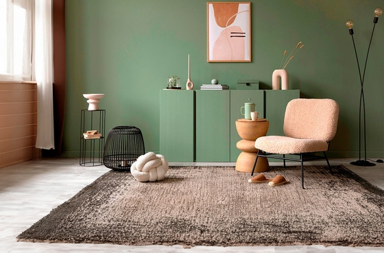 Mueble bajo en color verde con jarrón y sofá color crema